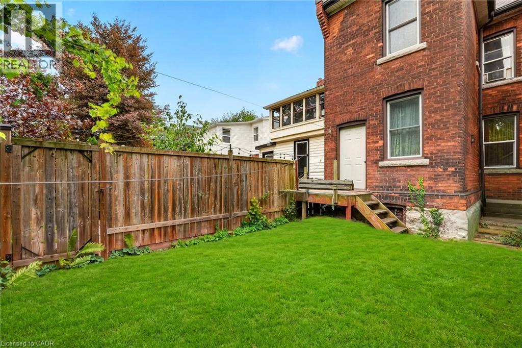 Expansive green lawn, wood privacy fence, red brick exterior, exterior wood deck, and exterior wood stairs - 199 N Locke Street N, Hamilton, ON