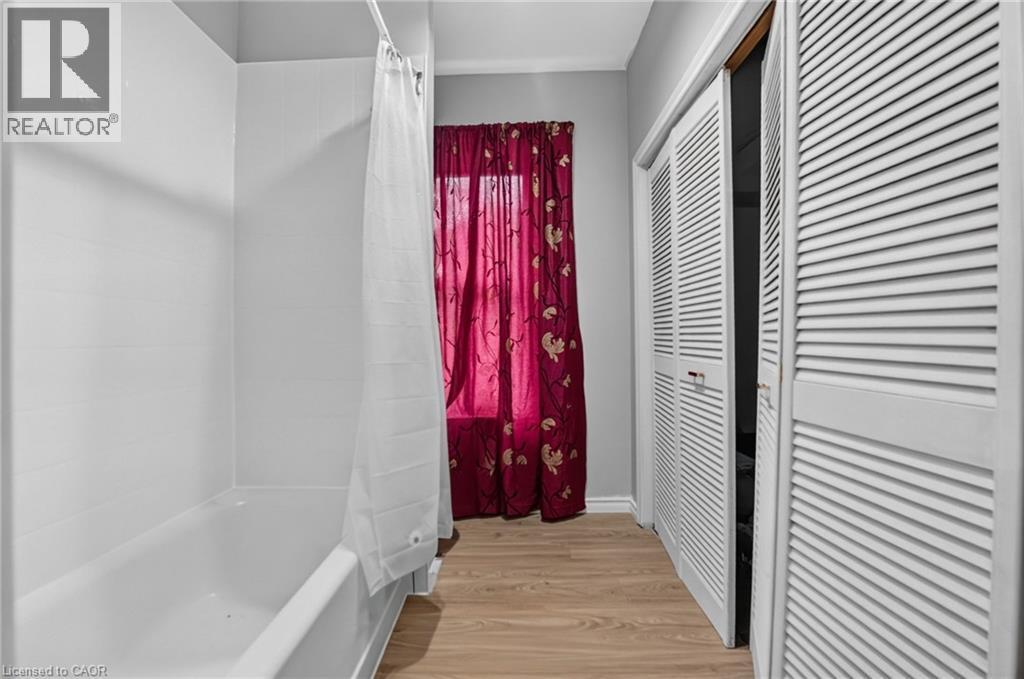 White tub with shower surround, wood-finish flooring, and white louvered bifold doors - 199 N Locke Street N, Hamilton, ON