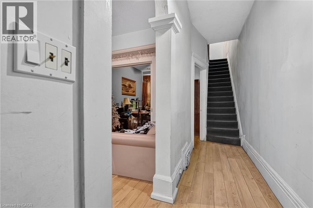 Hardwood-style flooring throughout the entry, staircase with dark carpeting, and white trim work - 199 N Locke Street N, Hamilton, ON