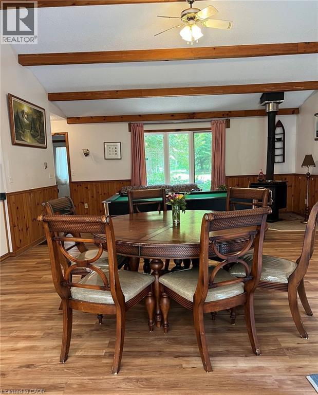 Vaulted ceiling with exposed wood beams, wood-finish flooring, wood paneling, ceiling fan light fixture, and a built-in wood stove - 16431 Highway 35, Algonquin Highlands, ON