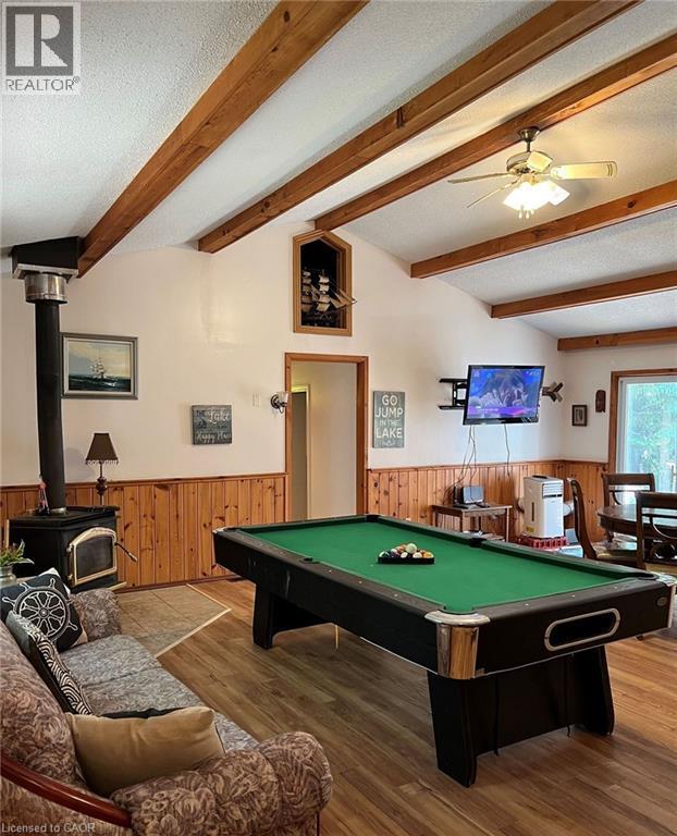 Vaulted ceiling with exposed wood beams, wood-finish flooring, wood paneling, and a corner wood-burning stove - 16431 Highway 35, Algonquin Highlands, ON
