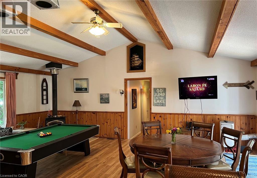 Vaulted ceiling with exposed wood beams, wood-finish flooring, wood-paneled wainscoting, and a freestanding wood-burning stove - 16431 Highway 35, Algonquin Highlands, ON