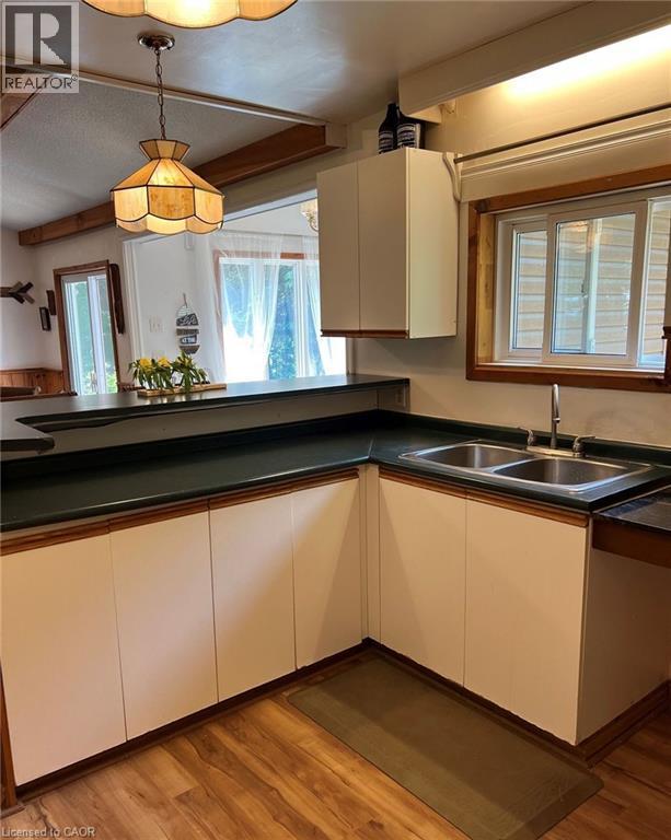 Kitchen featuring wood-finish flooring, white cabinetry with wood trim, dark countertops, and a double basin stainless steel sink - 16431 Highway 35, Algonquin Highlands, ON