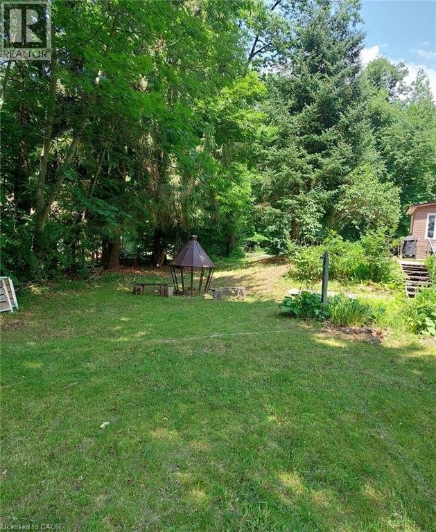 Expansive lawn area with a central fire pit structure and surrounding stone seating, bordered by mature trees and natural landscaping - 16431 Highway 35, Algonquin Highlands, ON