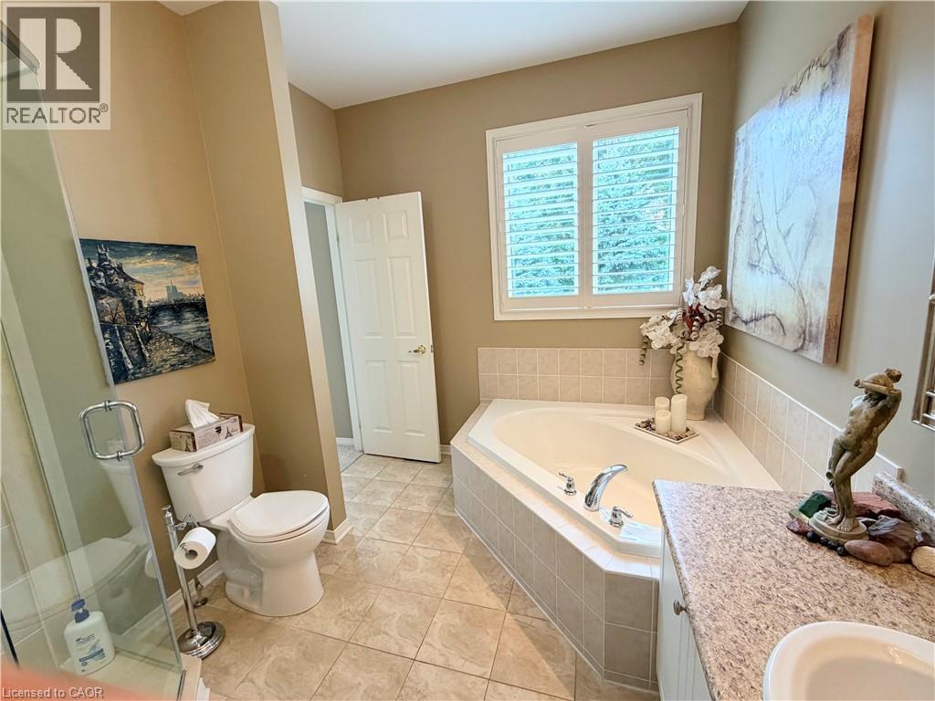 Corner soaking tub with tiled surround, plantation-style window shutters, and a granite-finish countertop vanity - 40 Stornoway Crescent, Huron East, ON