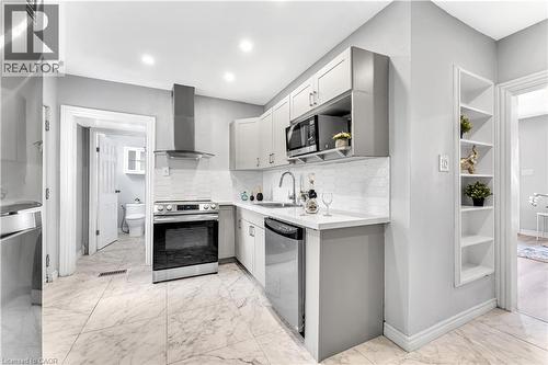Kitchen featuring stainless steel appliances, upper and lower cabinetry, an undermount sink, and a tiled backsplash - 101 Emerald Street N, Hamilton, ON 
