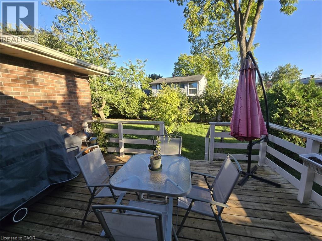 Expansive wood-finish deck with railing, bordering a manicured lawn and mature trees - 410 Lakeview Drive, Waterloo, ON