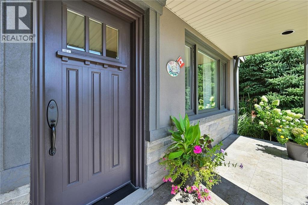 Recessed entryway featuring a paneled door with transom windows, a stone accent wall, and a covered porch with recessed lighting - 2209 Ghent Avenue, Burlington, ON
