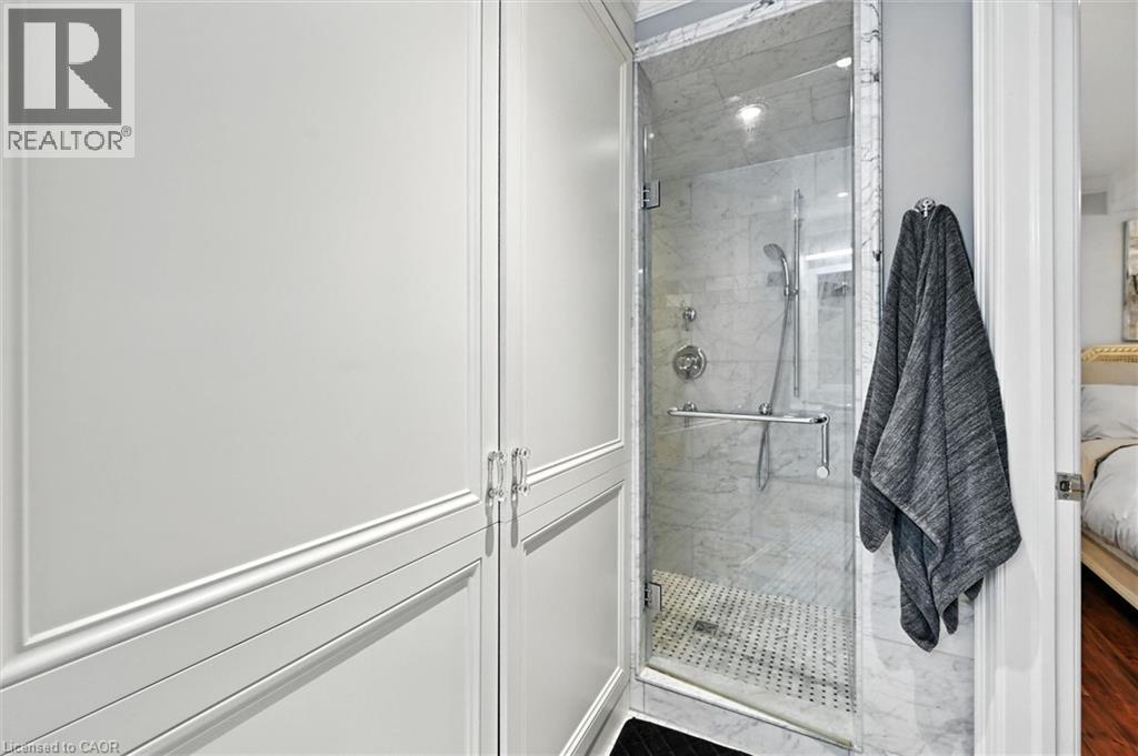 Glass-enclosed shower with marble-finish tile surround, fixed and handheld showerheads, and a tiled shower pan - 2209 Ghent Avenue, Burlington, ON