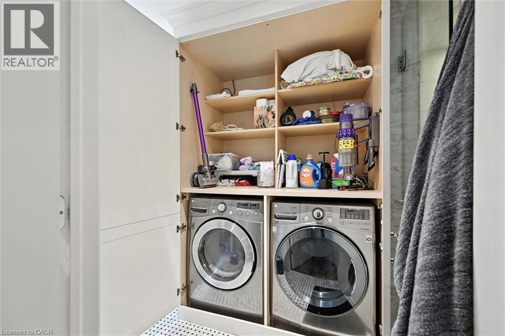 Built-in laundry closet featuring stacked appliances, integrated shelving, and white paneled doors - 2209 Ghent Avenue, Burlington, ON