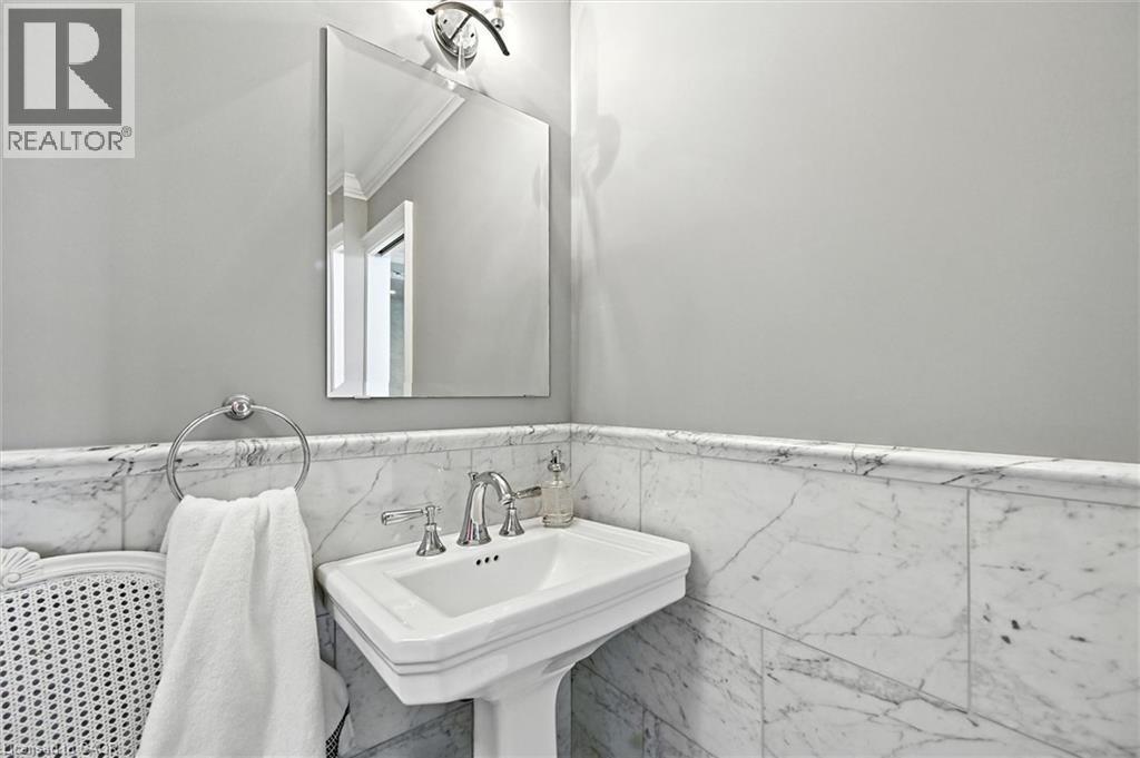 Pedestal sink with polished chrome fixtures, framed mirror, and marble wainscoting - 2209 Ghent Avenue, Burlington, ON