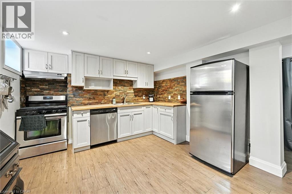 U-shaped kitchen with light wood-finish flooring, white cabinetry, a stone-tile backsplash, stainless steel appliances, and wood-finish countertops - 2209 Ghent Avenue, Burlington, ON