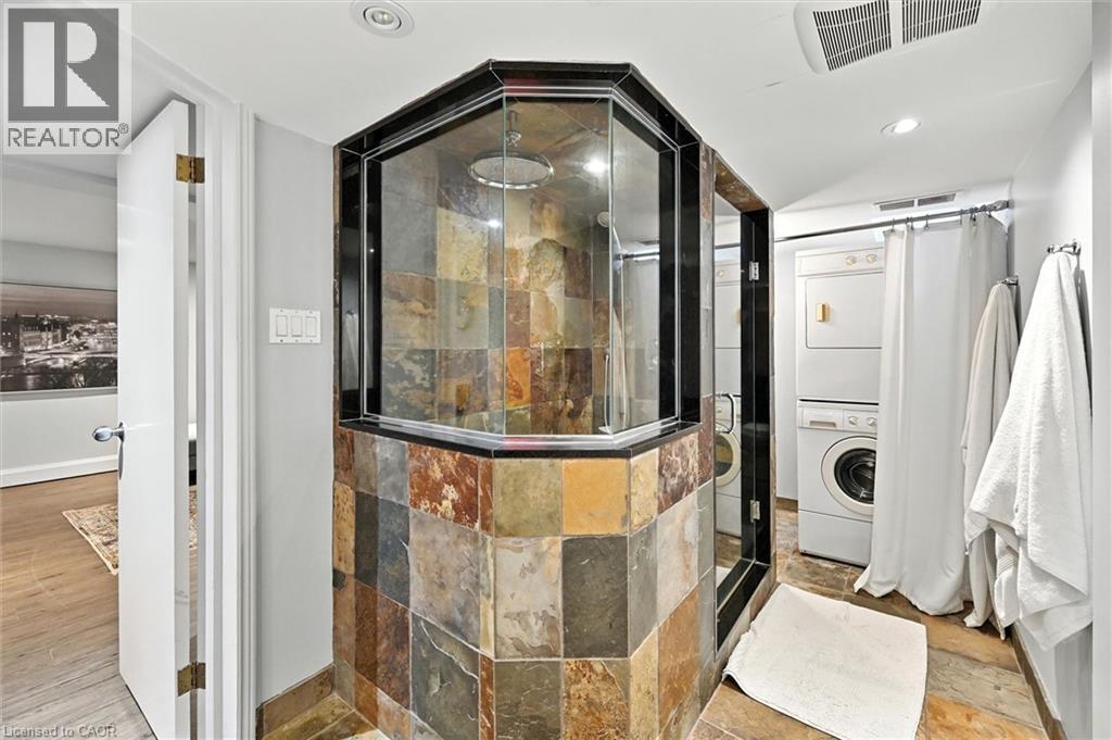 Glass-enclosed shower with stone tile surround, recessed lighting, and a stacked washer/dryer unit - 2209 Ghent Avenue, Burlington, ON