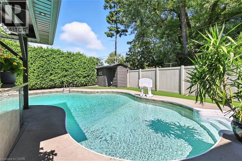 Swimming pool with integrated steps, concrete surround, privacy hedging, and an artificial turf area - 2209 Ghent Avenue, Burlington, ON