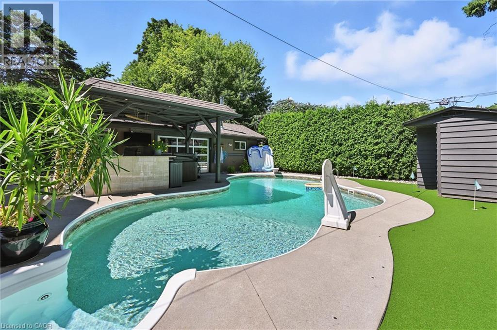 Curved swimming pool with concrete decking, covered outdoor bar area, and artificial turf putting green - 2209 Ghent Avenue, Burlington, ON