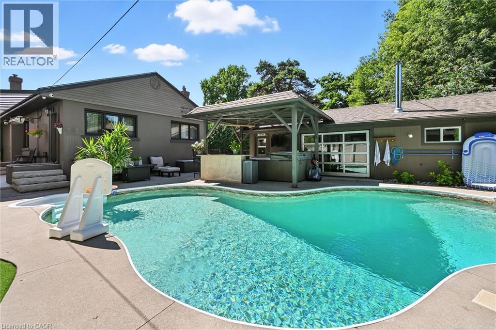 Curved swimming pool with integrated spa and surrounding concrete decking - 2209 Ghent Avenue, Burlington, ON