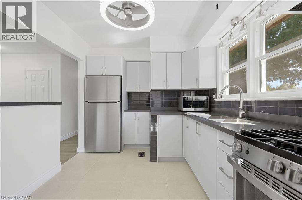Contemporary kitchen featuring white cabinetry, stainless steel appliances, dark gray countertops, and a subway tile backsplash - 49 Beverly Crescent, Welland, ON