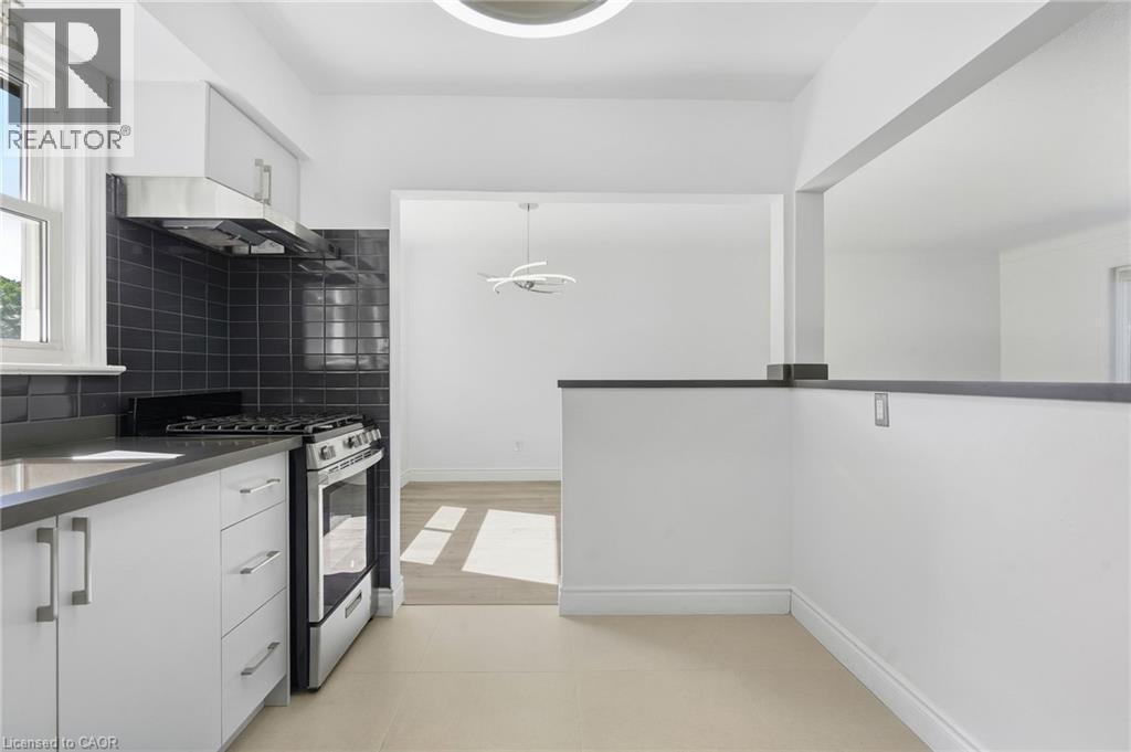 Kitchen featuring white cabinetry, stainless steel appliances, dark subway tile backsplash, and light tile flooring - 49 Beverly Crescent, Welland, ON