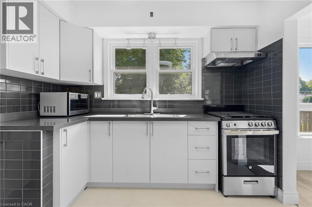 Kitchen featuring white cabinetry, dark subway tile backsplash, solid surface countertops, a stainless steel range, and a stainless steel range hood - 49 Beverly Crescent, Welland, ON