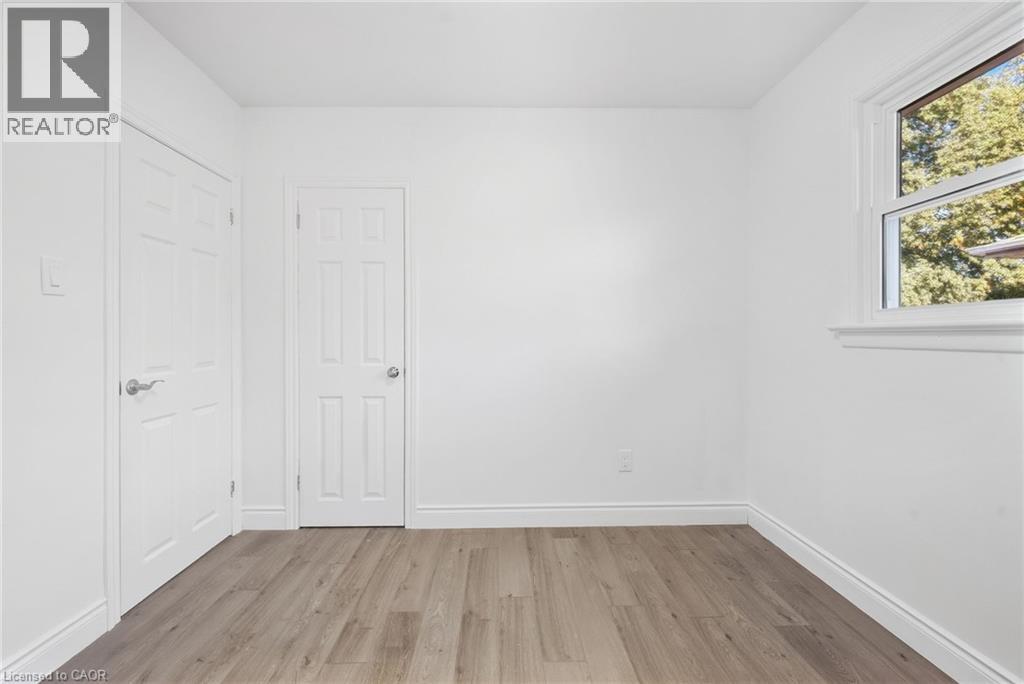 Wood-finish flooring with white trim, white paneled doors, and a white window frame with natural light - 49 Beverly Crescent, Welland, ON