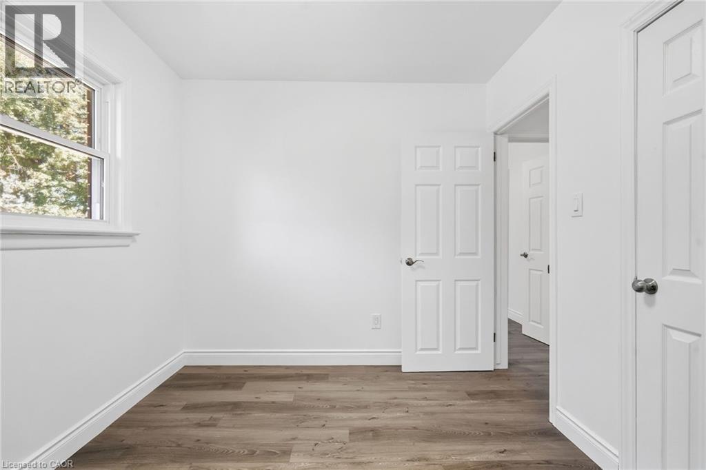 White interior walls with a window, wood-finish flooring, and a white paneled door - 49 Beverly Crescent, Welland, ON
