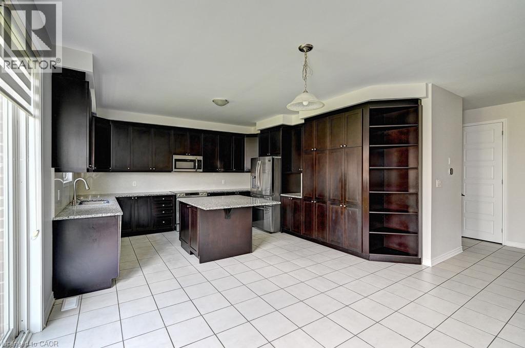 Kitchen featuring dark wood cabinetry, light-toned countertops, a central island, stainless steel appliances, and tile flooring - 236 Ridge Road, Cambridge, ON