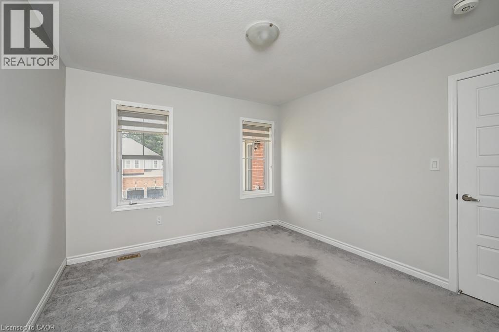 Neutral wall tones with gray carpeting, two windows with blinds, a flush mount ceiling light, and a paneled interior door - 236 Ridge Road, Cambridge, ON