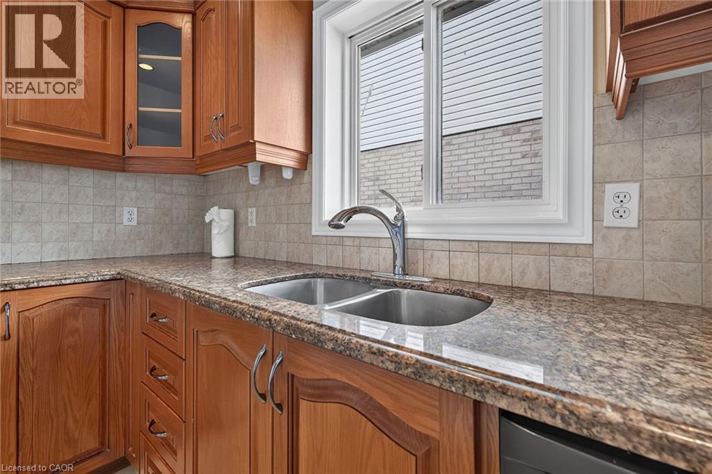 Wood-finish cabinetry, speckled countertop, tile backsplash, stainless steel double basin sink, and an integrated dishwasher - 795 Tenth Avenue, Hamilton, ON