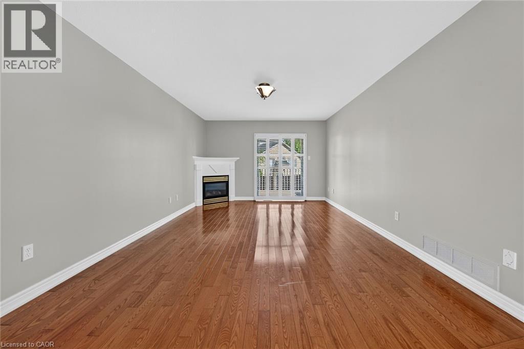 Hardwood flooring, a fireplace with a white mantel, light gray walls, white trim, and a patio door with exterior balcony railings - 795 Tenth Avenue, Hamilton, ON