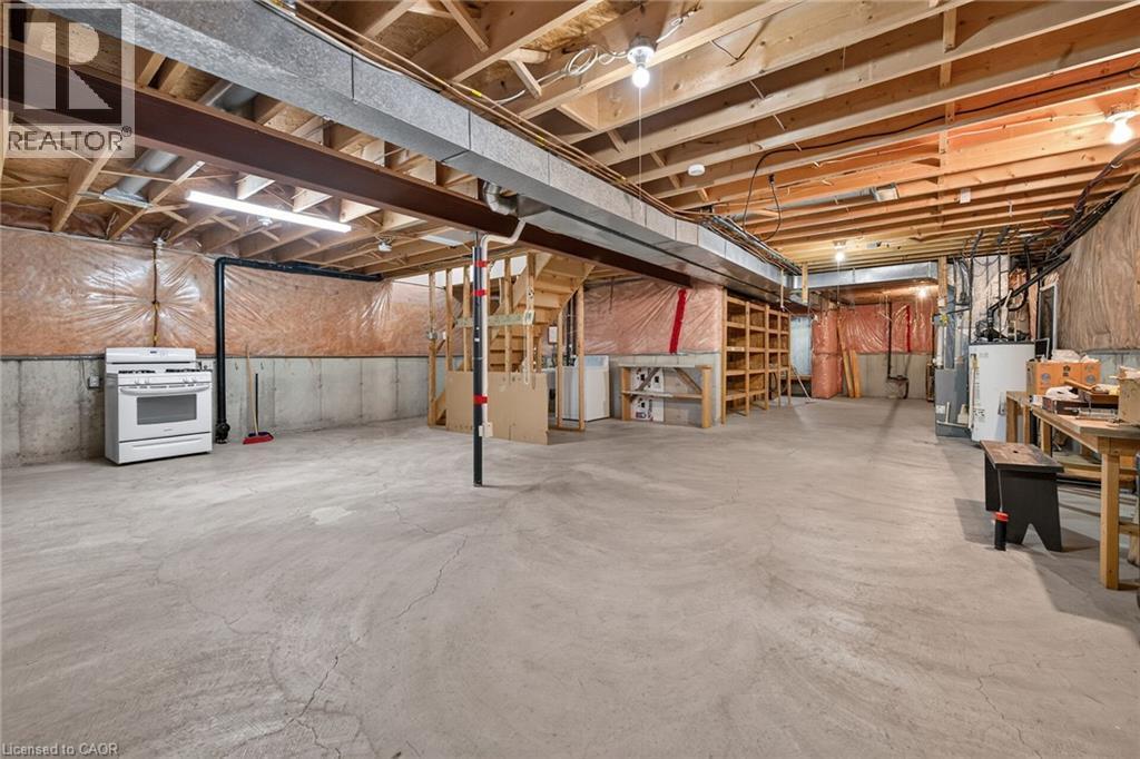 Expansive unfinished basement featuring concrete flooring, exposed wood ceiling joists, and a built-in shelving unit - 795 Tenth Avenue, Hamilton, ON