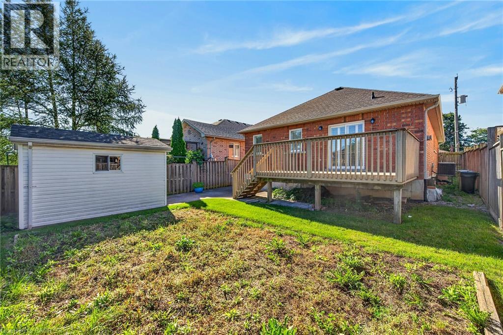 Expansive backyard featuring a wood deck, red brick exterior, white vinyl-sided shed, and wood fencing - 795 Tenth Avenue, Hamilton, ON