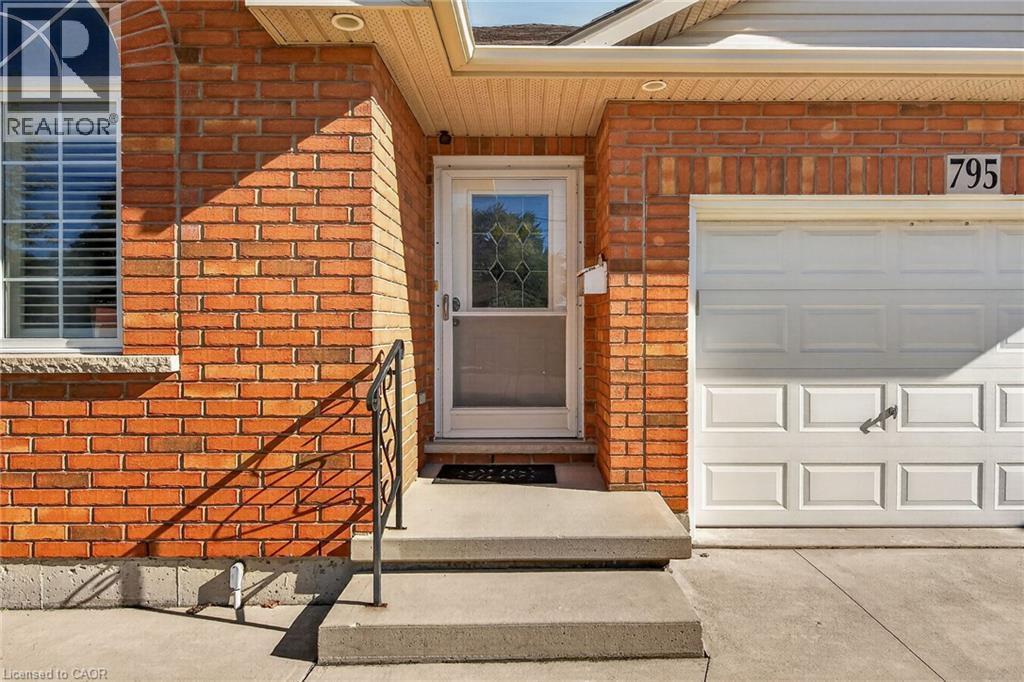 Brick exterior with an arched window, white garage door, concrete steps, and a wrought iron handrail - 795 Tenth Avenue, Hamilton, ON