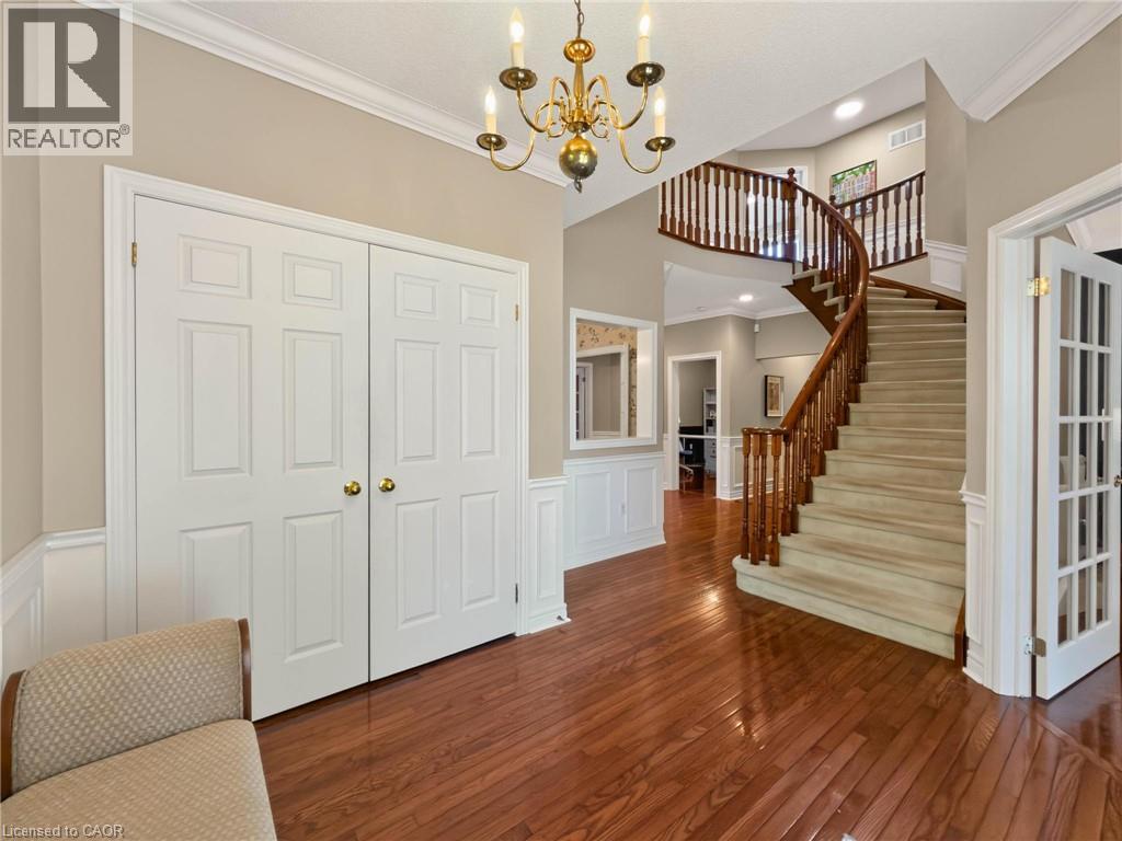 Grand foyer featuring hardwood flooring, a curved staircase with wood banister, wainscoting, and a brass chandelier - 74 Davidson Boulevard, Dundas, ON