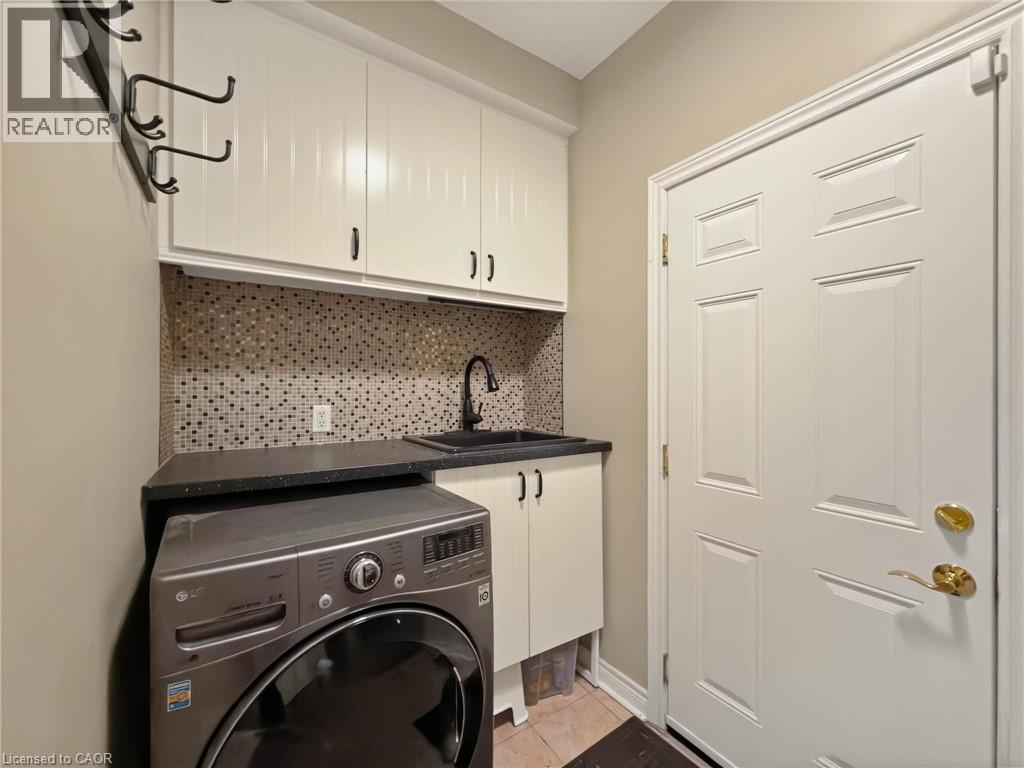 Upper cabinetry, mosaic tile backsplash, integrated utility sink with dark countertop, and paneled entry door - 74 Davidson Boulevard, Dundas, ON