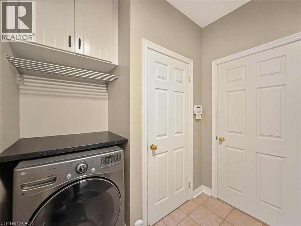 Laundry area featuring overhead cabinetry, a wall-mounted drying rack, a black countertop, and tile flooring - 74 Davidson Boulevard, Dundas, ON