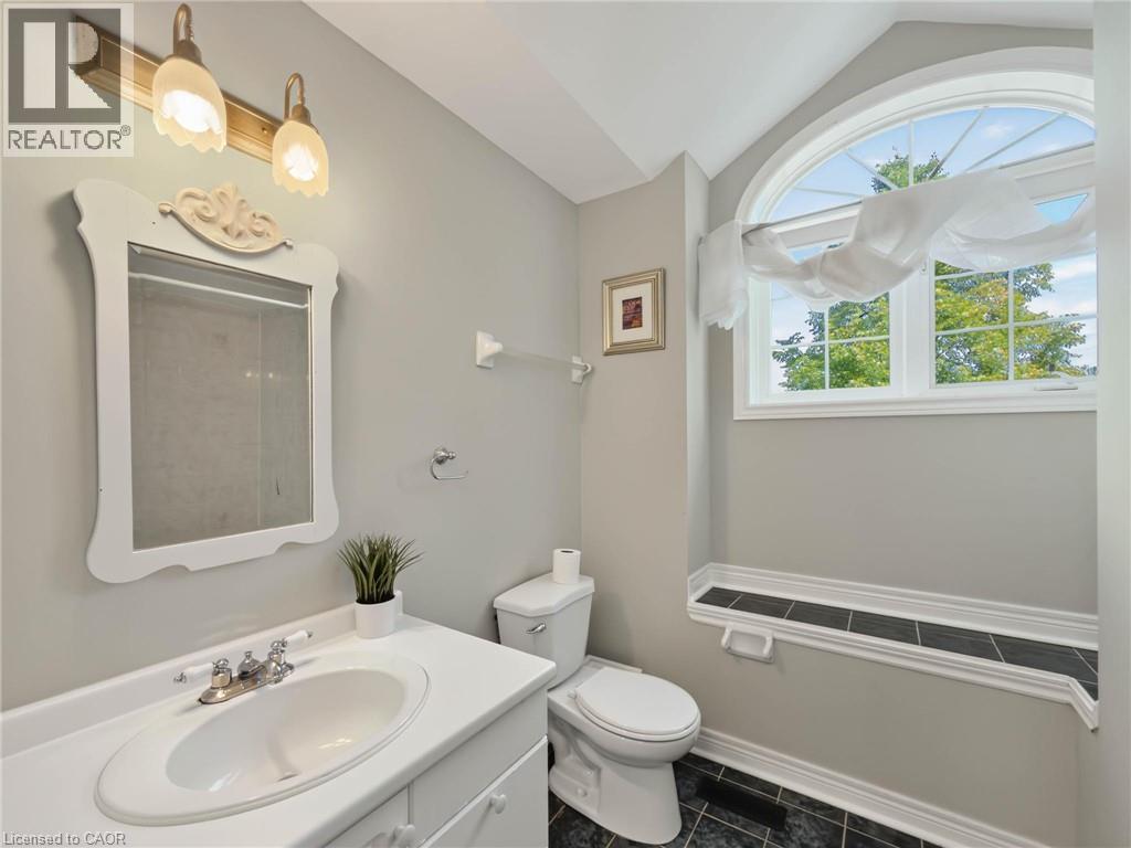Bathroom featuring a white vanity with an integrated sink, a decorative mirror, and a toilet - 74 Davidson Boulevard, Dundas, ON