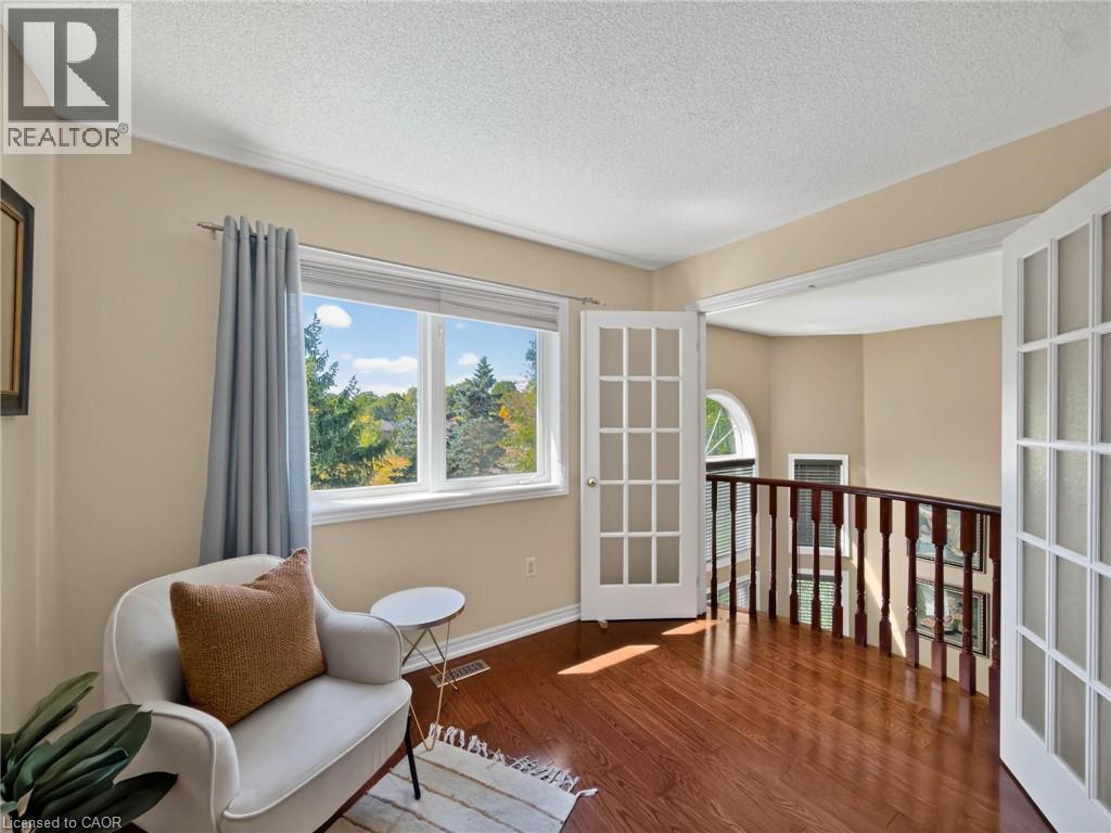 Expansive window with natural scenery, rich wood-finish flooring, white French doors, detailed wood railing, and crown molding - 74 Davidson Boulevard, Dundas, ON