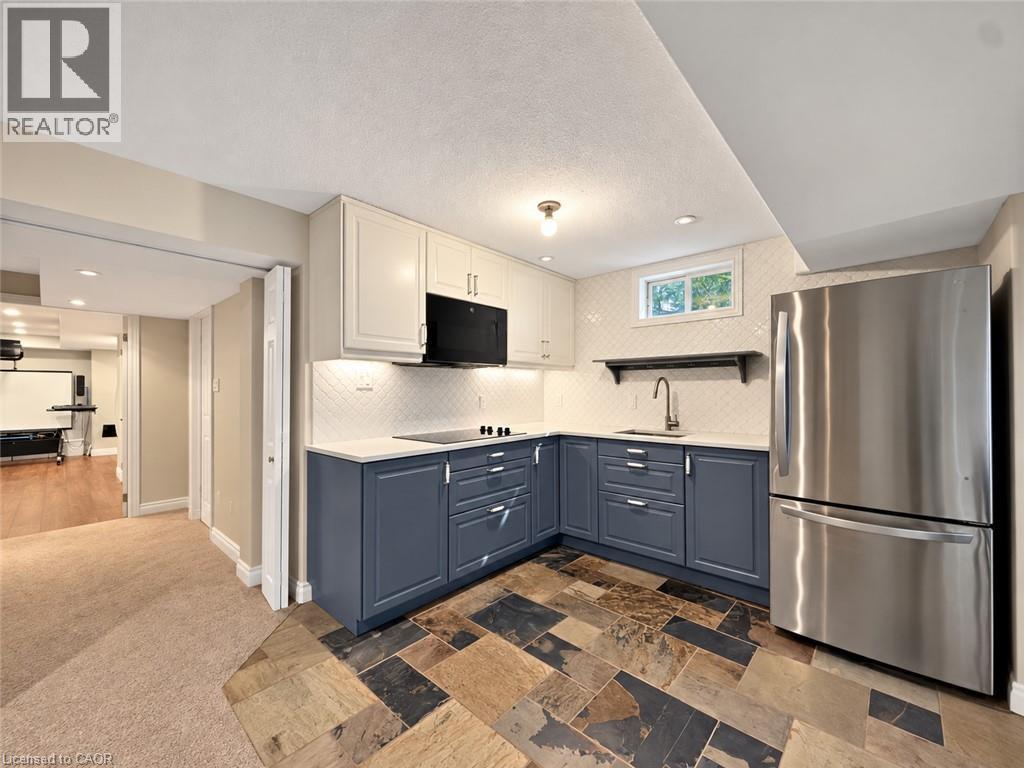Kitchenette with stainless steel refrigerator, white upper cabinetry, blue lower cabinetry, and a tile backsplash - 74 Davidson Boulevard, Dundas, ON