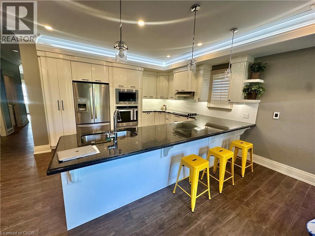 Gourmet kitchen featuring stainless steel appliances, dark stone countertops, wood-finish flooring, white subway tile backsplash, and recessed lighting - 5 Arden Avenue, Hamilton, ON