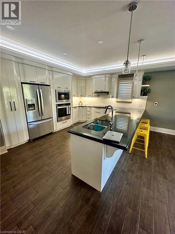 Kitchen featuring dark wood-finish flooring, white cabinetry, dark countertops, a stainless steel refrigerator, and pendant lighting - 5 Arden Avenue, Hamilton, ON