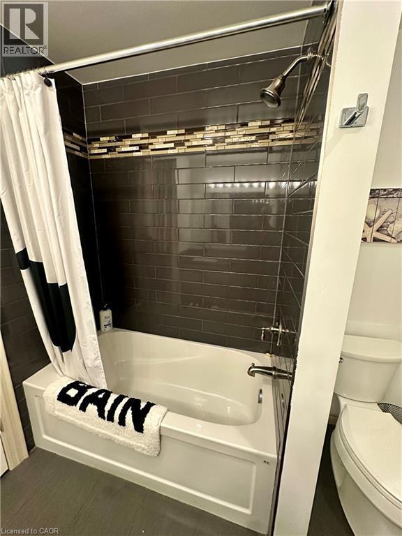 Bathtub with a shower fixture, dark subway tile surround, and decorative mosaic tile accent band - 5 Arden Avenue, Hamilton, ON