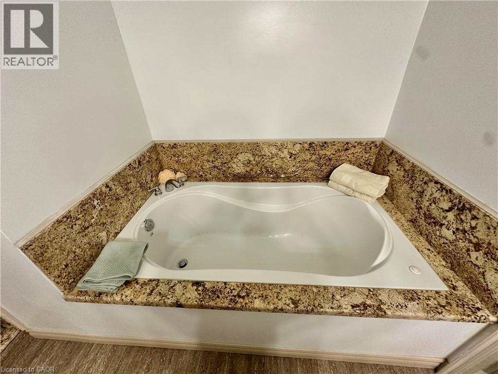 Built-in soaking tub with a stone-finish surround, wall-mounted fixtures, and wood-finish flooring - 5 Arden Avenue, Hamilton, ON