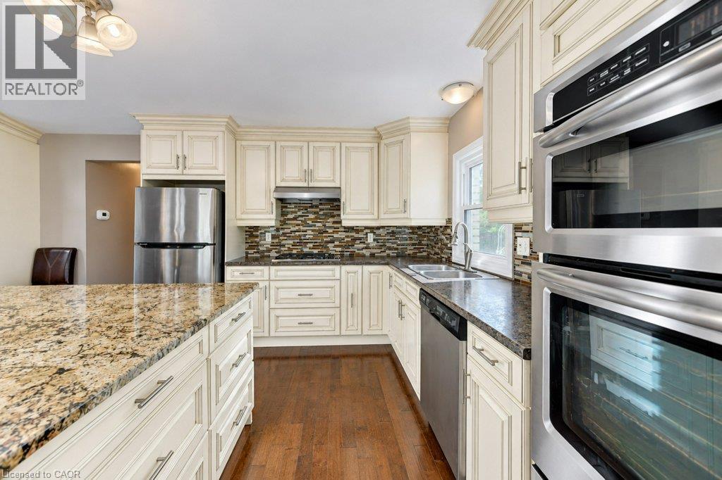 Kitchen featuring white cabinetry, granite countertops, stainless steel appliances, a tile backsplash, and wood-finish flooring - 34 Wayne Drive, Kitchener, ON