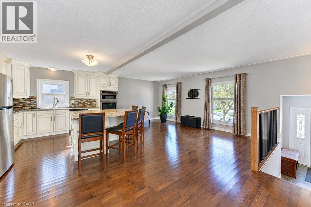 Expansive wood-finish flooring throughout, kitchen with white cabinetry, stainless steel appliances, and a tiled backsplash, and a staircase with black spindles - 34 Wayne Drive, Kitchener, ON