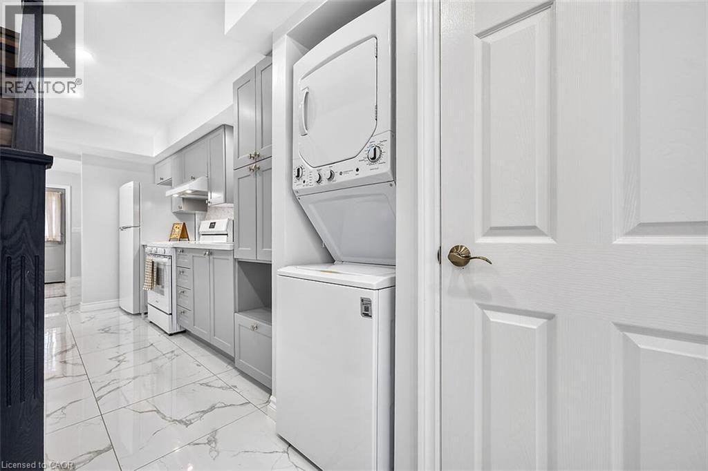 Compact kitchen featuring light gray cabinetry, white appliances, and a stackable washer and dryer unit - 4 Albemarle Street, Hamilton, ON