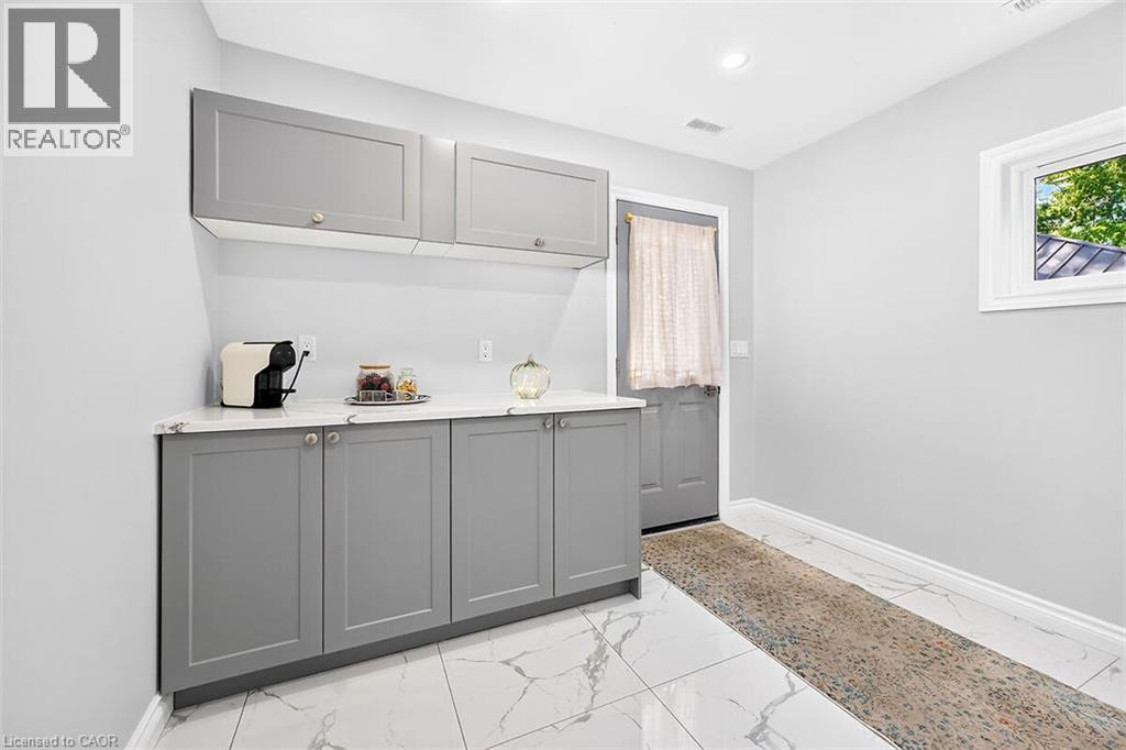 Gray shaker-style cabinetry with gold-tone hardware, white countertop, white tile flooring with gray veining, recessed ceiling lighting, and a white-framed window - 4 Albemarle Street, Hamilton, ON
