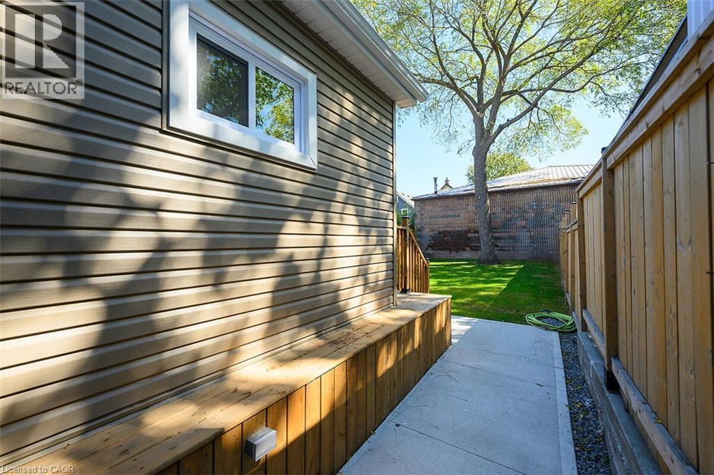 Side exterior showcasing horizontal siding, a sliding window, a concrete pathway, a wooden privacy fence, and a grassy area with a mature tree - 4 Albemarle Street, Hamilton, ON
