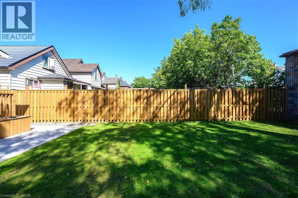 Expansive grassy yard with a wooden privacy fence, concrete path, and a built-in wooden planter - 4 Albemarle Street, Hamilton, ON