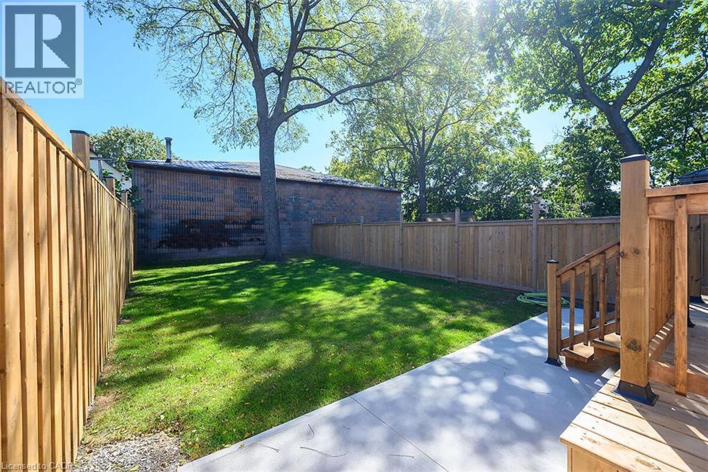 Expansive backyard featuring a manicured lawn, concrete patio, and a wood deck with stairs - 4 Albemarle Street, Hamilton, ON