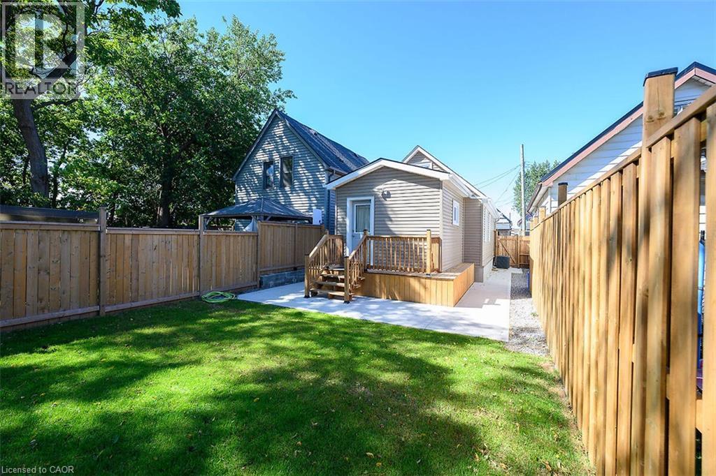 Expansive green lawn with a wooden privacy fence, concrete patio, and a raised wooden deck with stairs - 4 Albemarle Street, Hamilton, ON